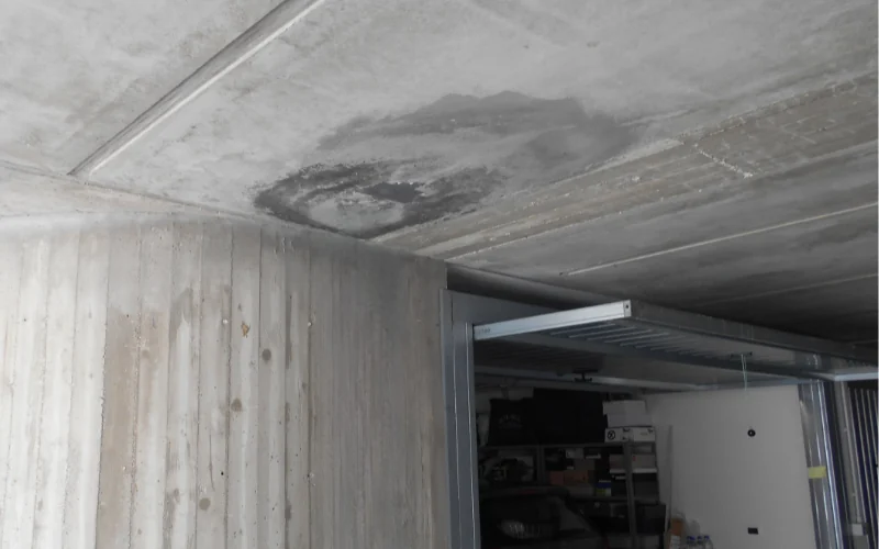 Soffitto di un garage interrato con macchie scure di infiltrazione.