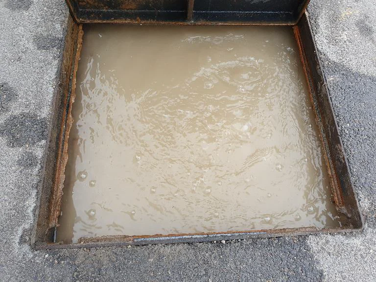 Pozzetto d'ispezione pieno d'acqua torbida, con bolle in superficie.